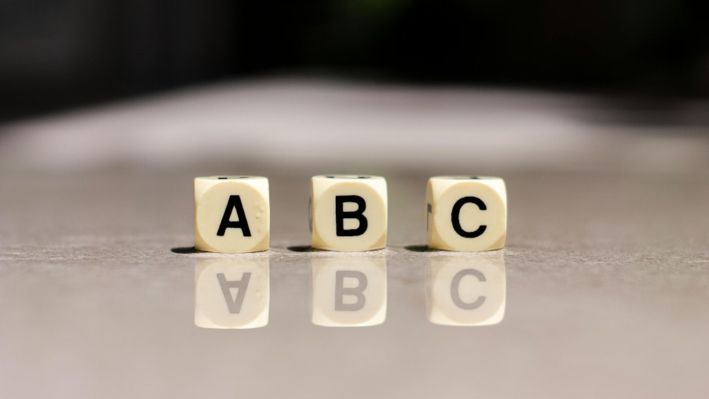 Three cubes with the letters A, B and C are standing on a grey surface.