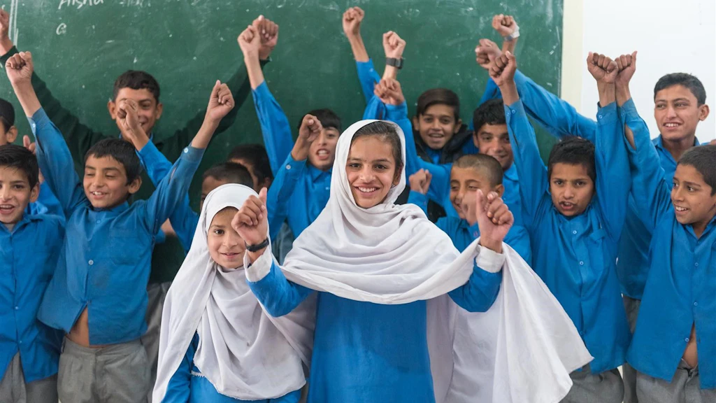 Eine Schulklasse in Pakistan steht vor einer Tafel und hat Freude.