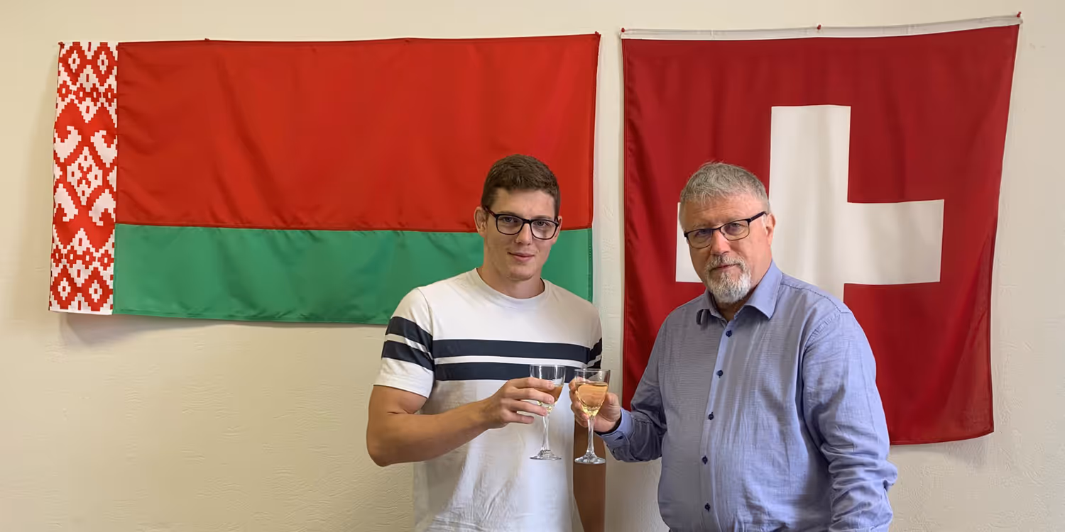 Zwei Männer stehen vor einer Wand mit den Flaggen von Belarus und der Schweiz.