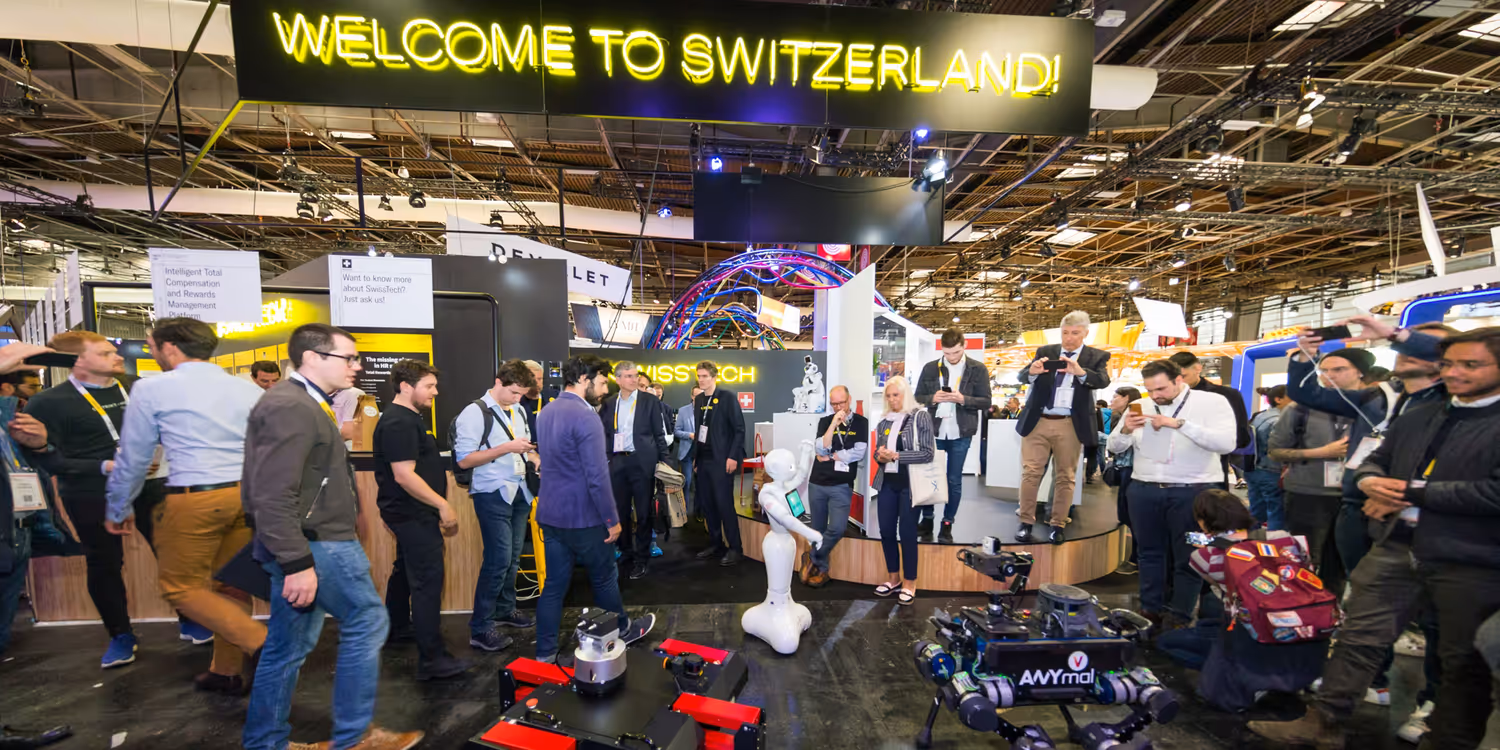 In einer Ausstellungshalle schauen sich Menschen Drohnen, Roboter und innovative Technologien an. Oben steht ein Schild mit der Aufschrift «Welcome to Switzerland».