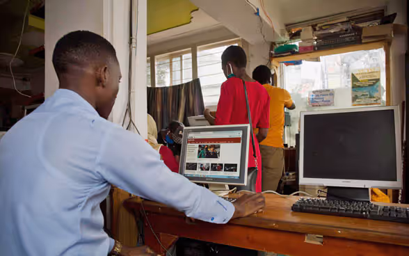 Ein afrikanischer Mann sitzt hinter einem Computer und liest online Zeitung.