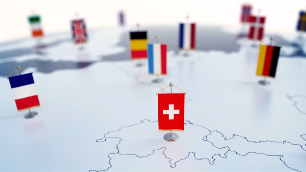 Karte von Europa mit kleinen Fahnen, die verschiedene Länder markieren, im Vordergrund die Schweizer Flagge.