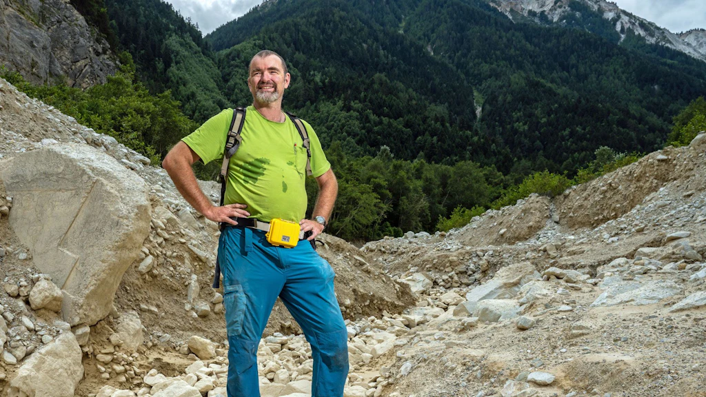 Eric Bardou steht auf einer Geröllhalde, im Hintergrund sieht man Berge.