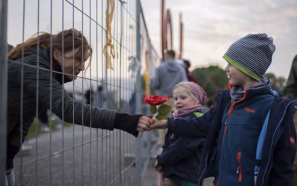 Eine Frau reicht durch den wegen der Pandemie errichteten Grenzzaun in Konstanz zwei Kindern eine Blume.