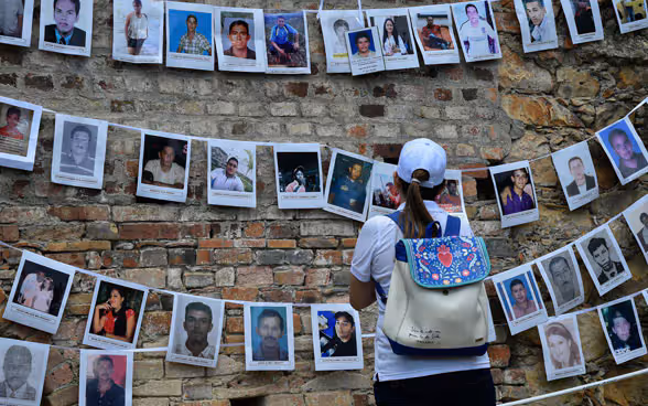 Eine Frau steht vor einer Wand mit Fotos von vermissten Personen.