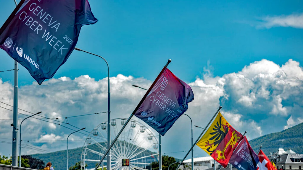 Auf dem Bild sind die Fahnen der 'Geneva Cyber Week 2025' in Genf, mit Riesenrad und Berglandschaft im Hintergrund zu sehen.