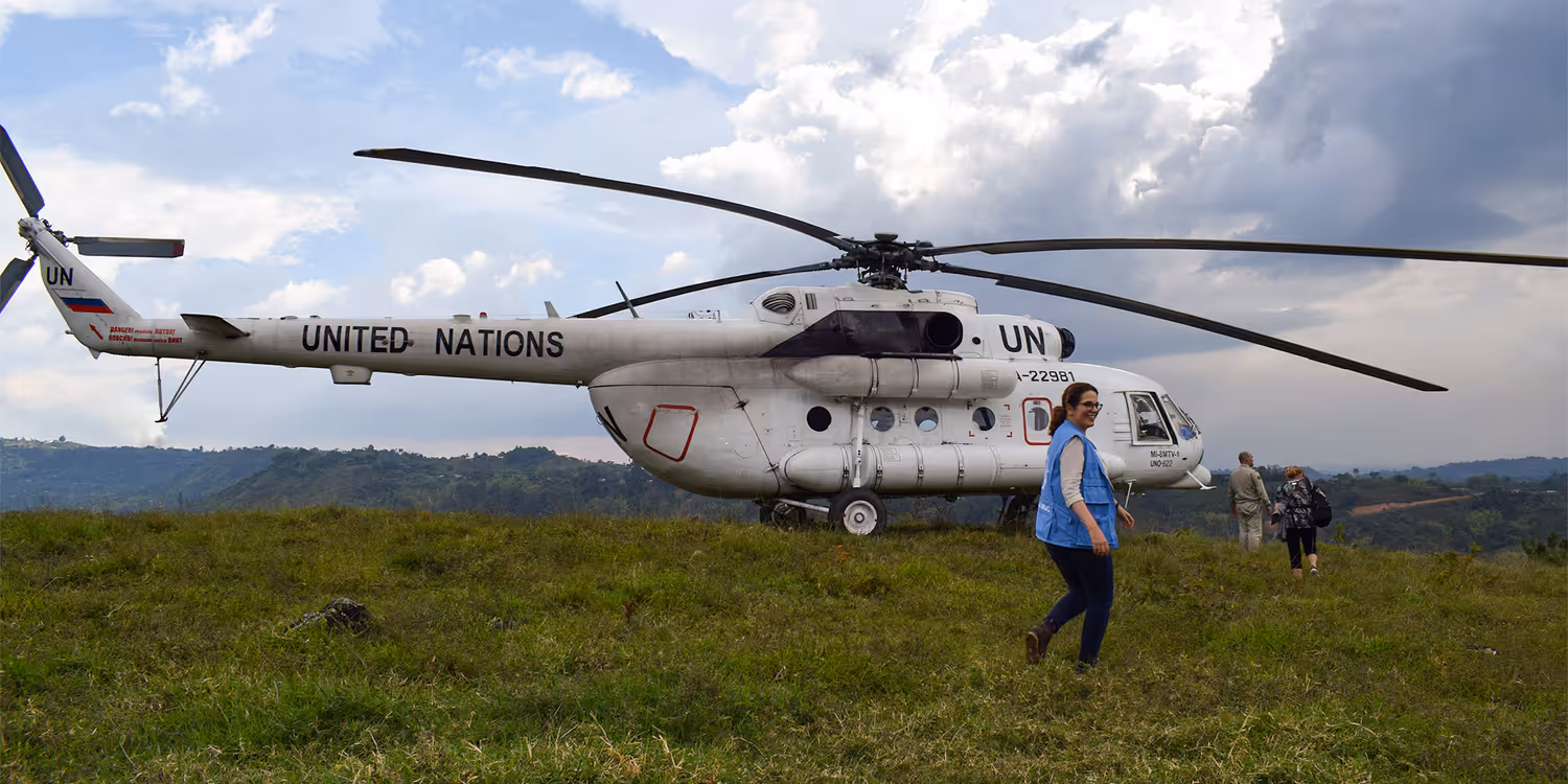 Natalie Kohli vor einem UN-Hubschrauber, der auf einer grünen Wiese hält.