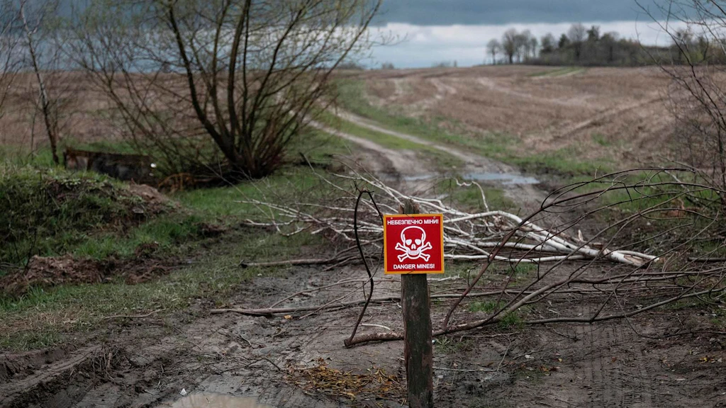 Ein rotes Schild mit einem Totenkopf steht auf einem Weg und warnt vor einem Minenfeld.