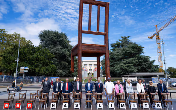 Männer und Frauen stehen auf der Place des Nations in Genf vor Stühlen, auf denen geschrieben steht «War has limits».