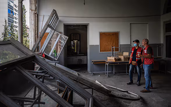 Zwei Experten der Humanitären Hilfe des Bundes blick aus einer kaputten Wand eines Klassenzimmers.