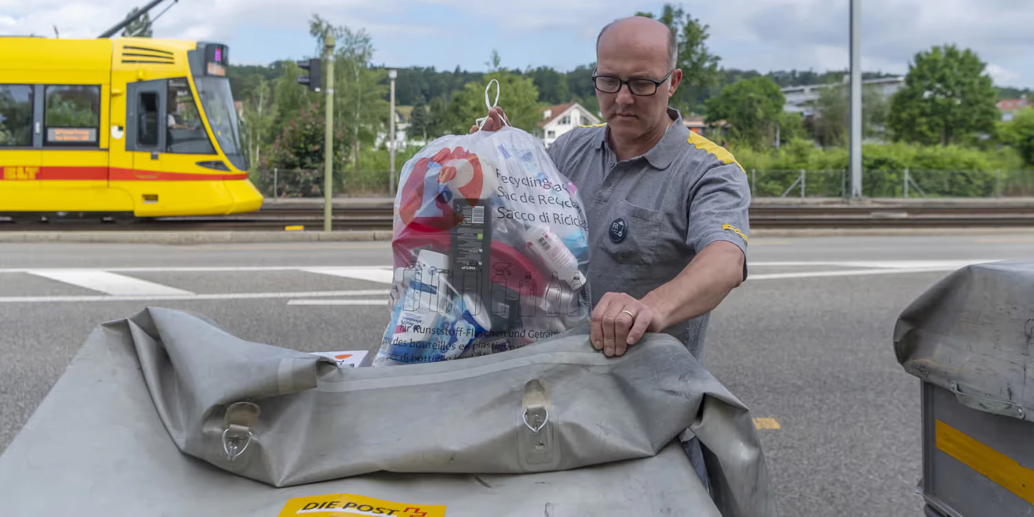 Ein Pöstler verstaut einen Recycling-Sack mit leeren Kunststoffflaschen und Getränkekartons in seinem Karren.