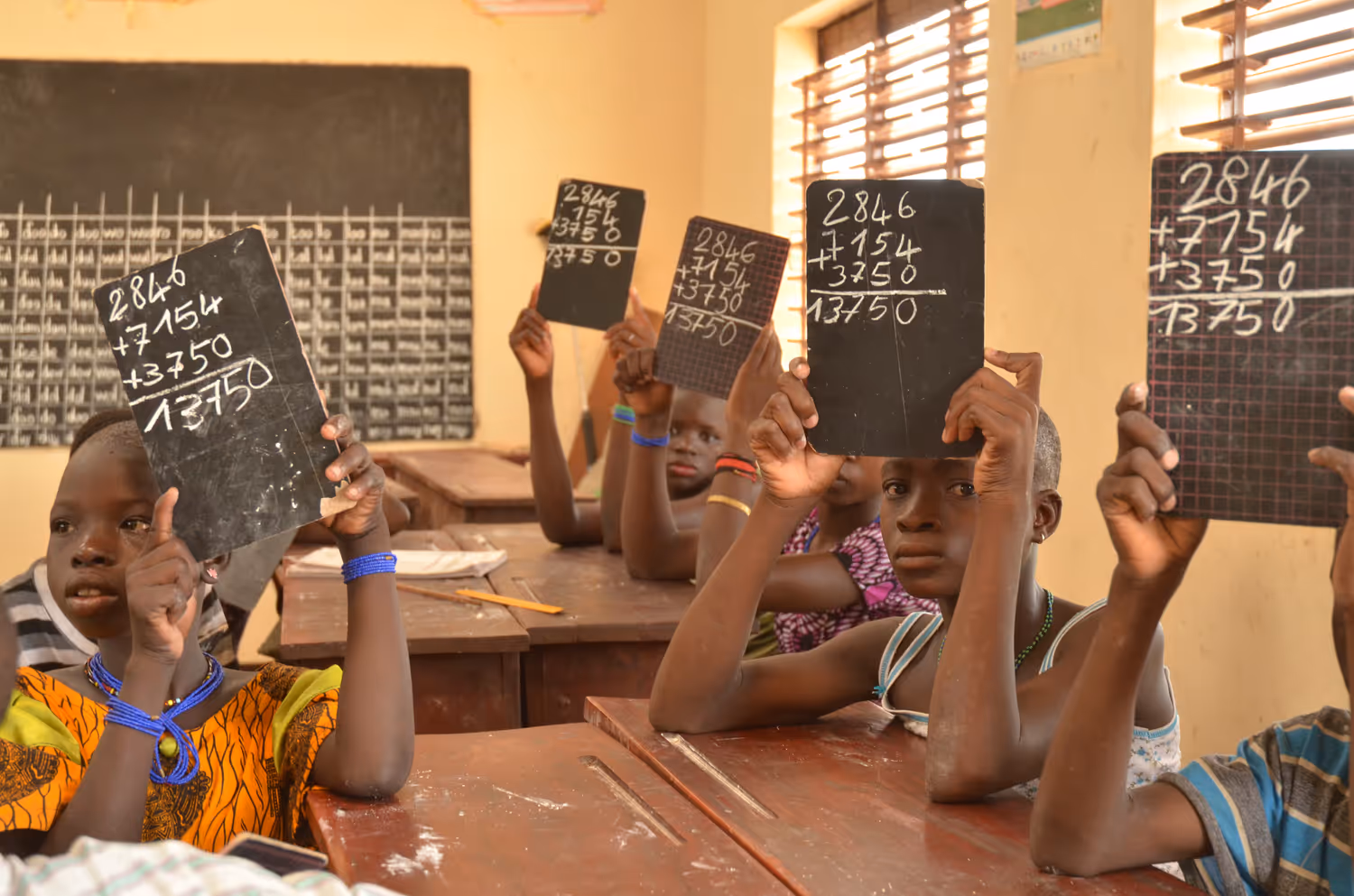 Afrikanische Schüler halten in einem Schulzimmer Kreidetafeln mit einer Rechnung in die Höhe.