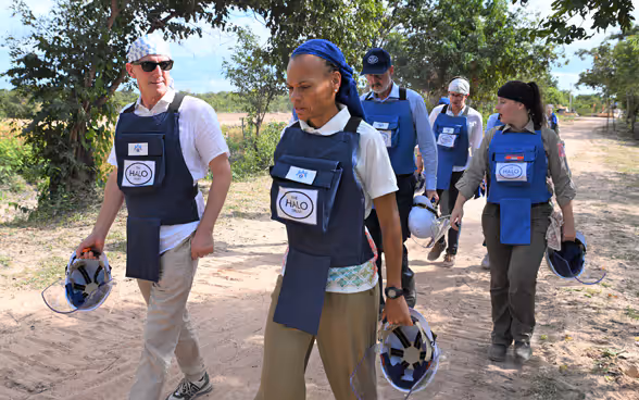 Eine Gruppe von Personen in Schutzausrüstung laufen auf einem Schotterweg, der zu einem Minenfeld führt. 