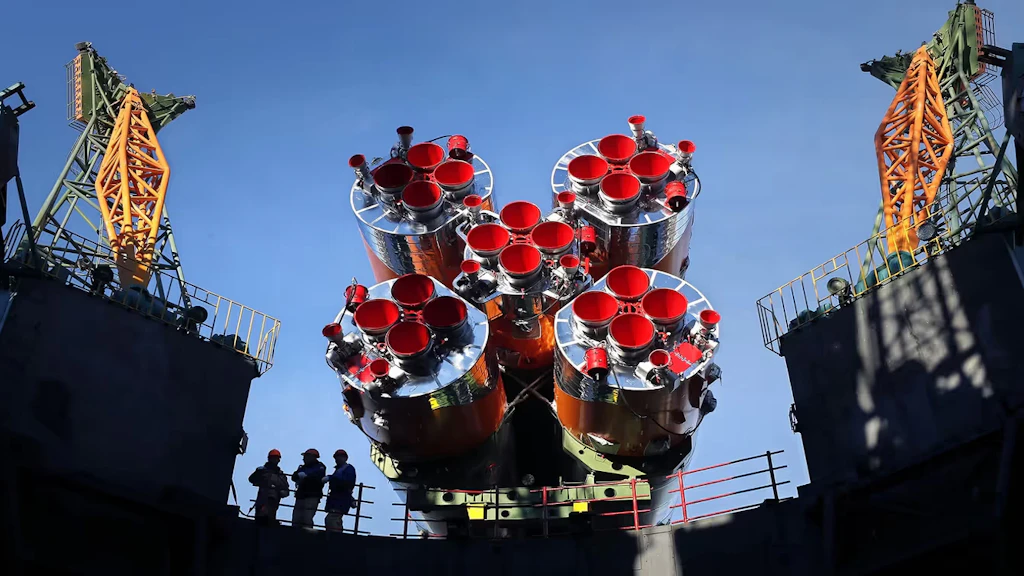 Das Triebwerk einer Rakete neben einer Abschussrampe bei stahlblauem Himmel.