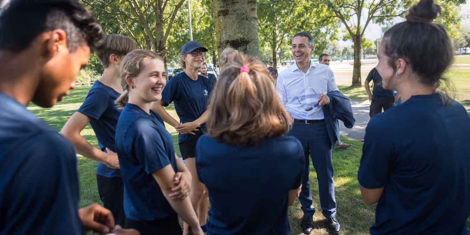 Bundesrat Ignazio Cassis im Gespräch mit Leichtathletinnen und Leichtathleten beim Training.