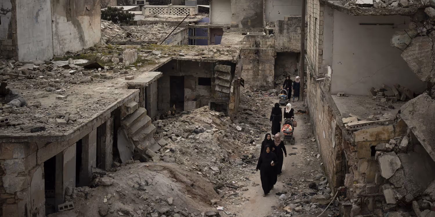 Frauen laufen mit Kinderwagen durch die Trümmer einer Strasse mit eingestürzten Häusern.