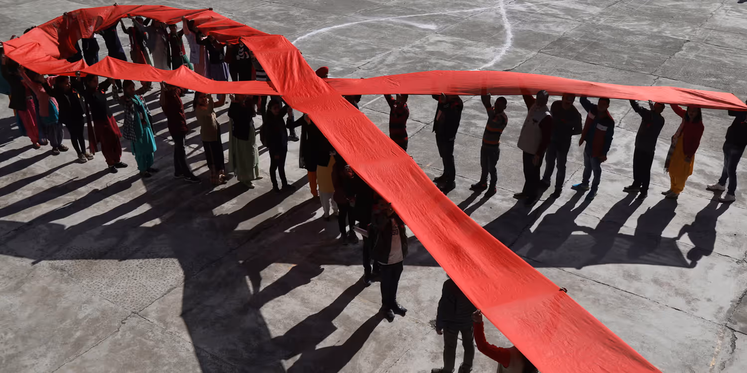 People lined up in the shape of a bow, raising a long red ribbon above their heads to form the internationally recognised symbol of the fight against AIDS.