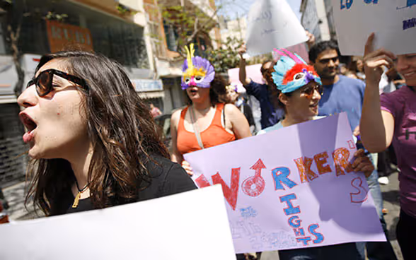 A group of people is demonstrating in the street holding signs saying "Worker's rights".