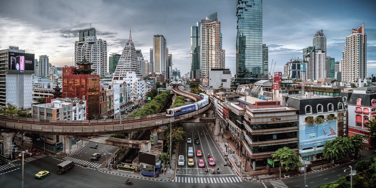 A train travels over a road with buildings in the background.