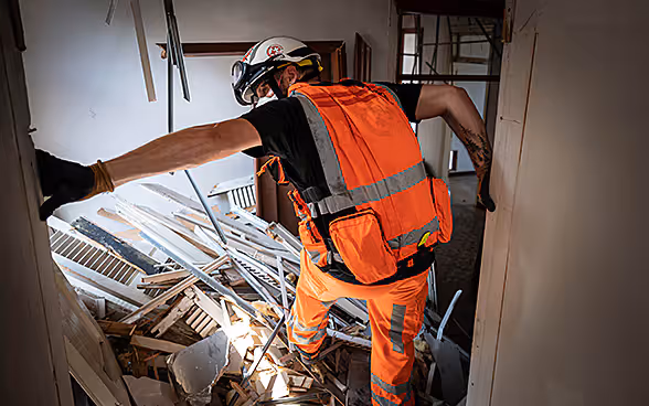 An expert from the Swiss Humanitarian Aid Unit is climbing over debris in a house. 