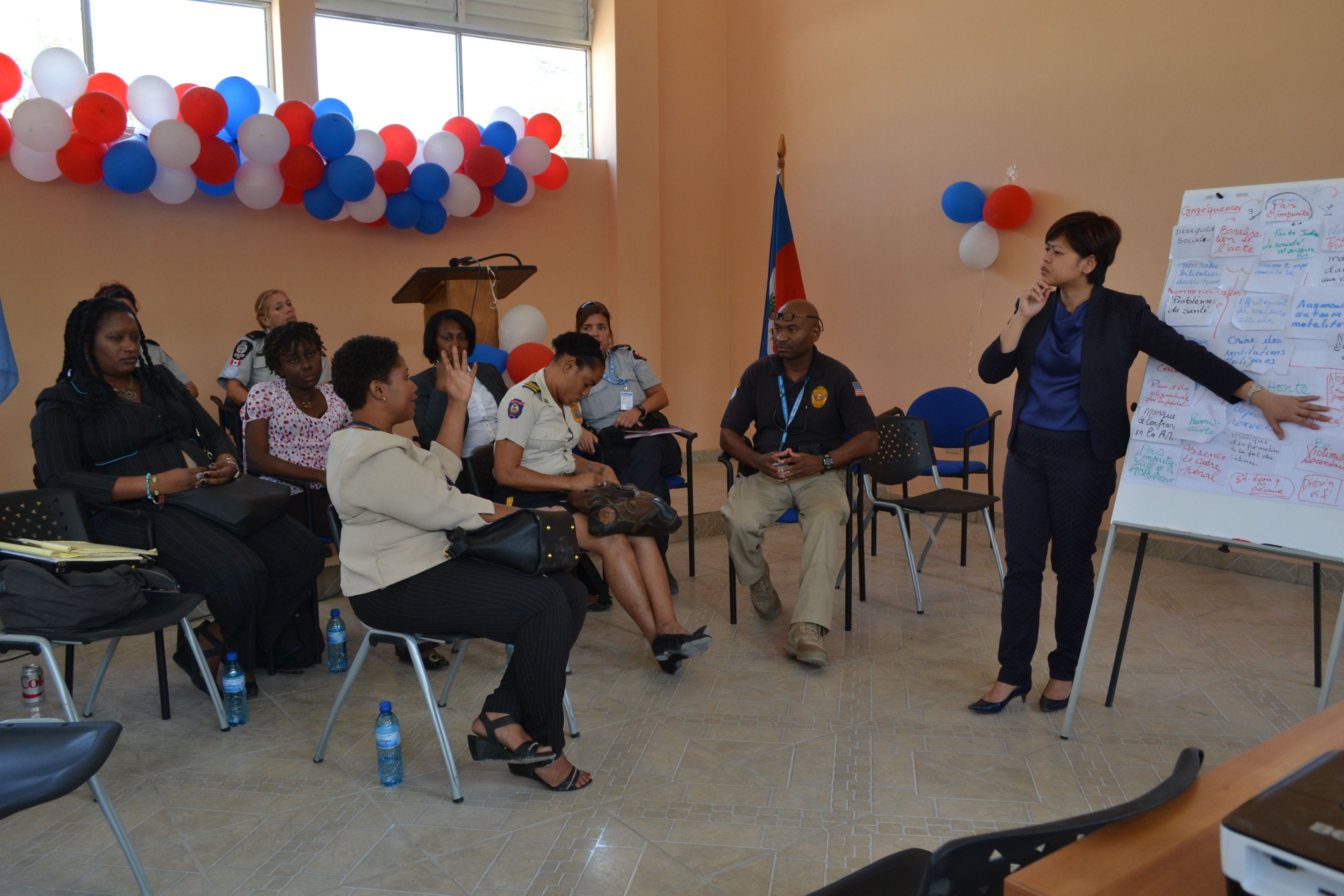 A woman standing in front of a flipchart, teaching a group of men and women sitting in front of her.