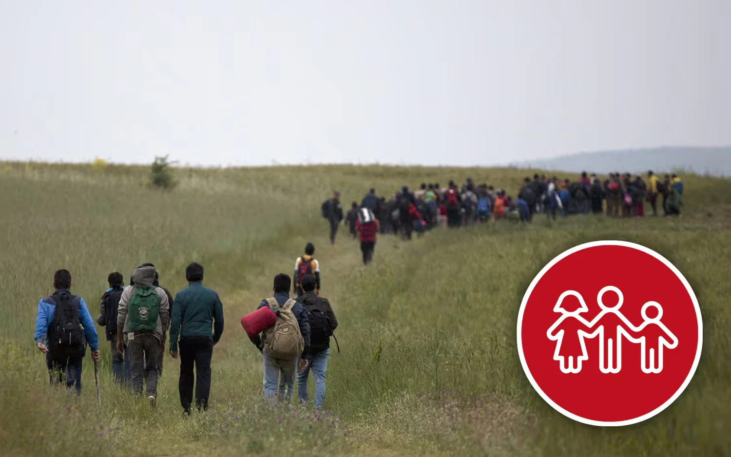 A group of refugees walks across a field through dense grass.