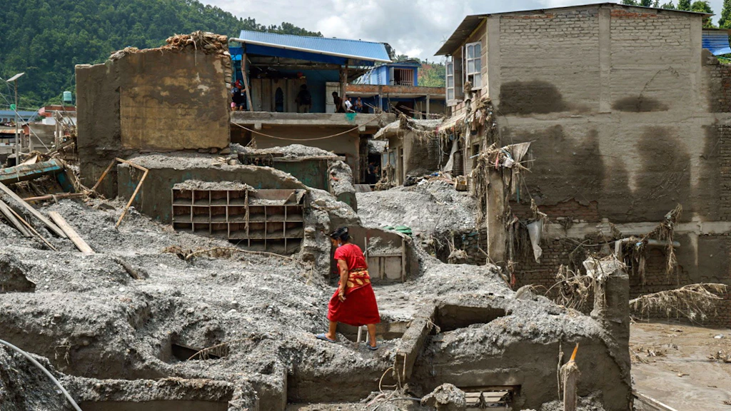 A woman climbs over the rubble of a destroyed house.
