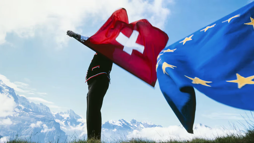A flag-thrower waving the Swiss flag in one hand and the EU flag in the other against the backdrop of the Bernese Alps.