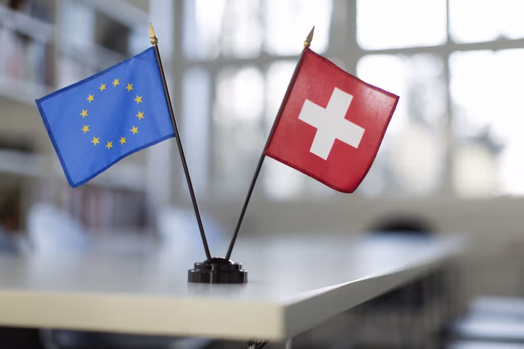 The Swiss and EU flags standing on a white table.