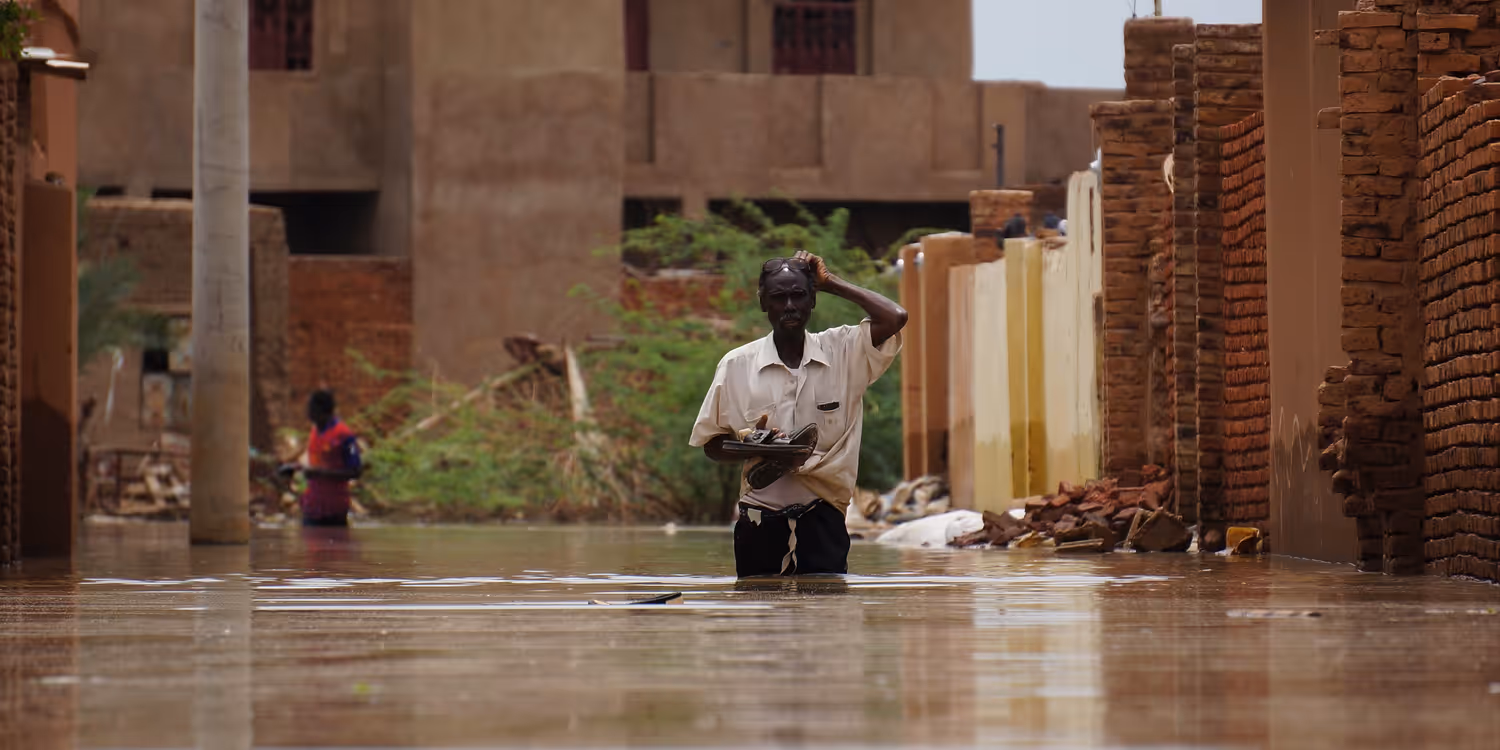 A man walks down a street, his legs completely submerged by water.
