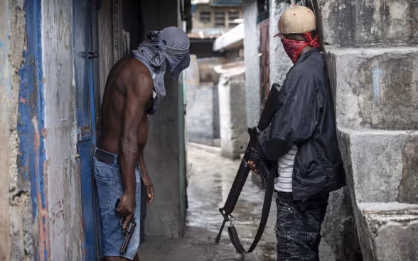 Two gang members stand armed with a revolver and a rifle in a narrow alley in Port-au-Prince, the capital of Haiti.