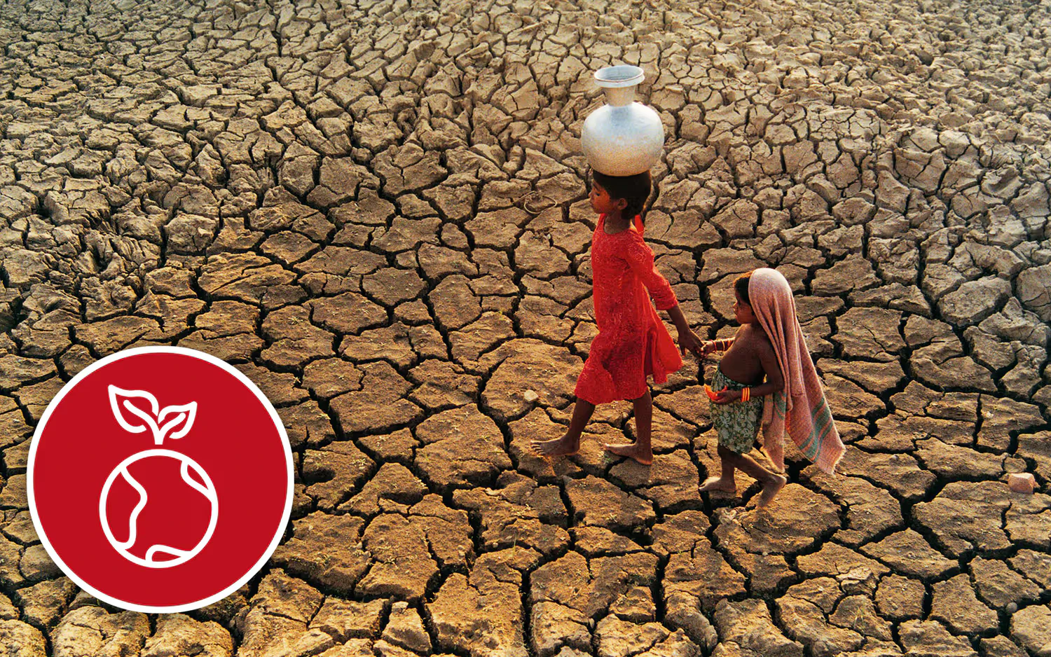 Two children walk across a dried-out river bed with a pitcher of water.