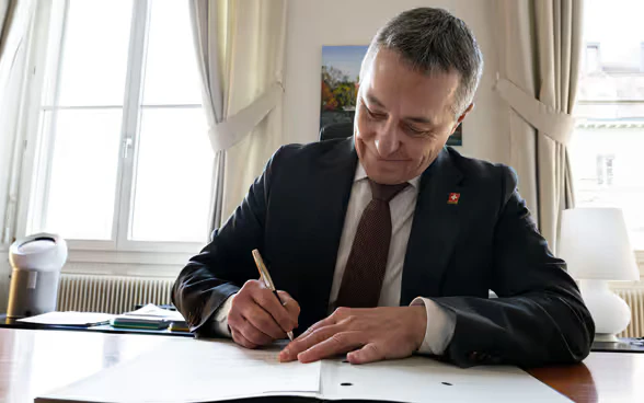 Federal Councillor Ignazio Cassis sits at a table and signs a document.