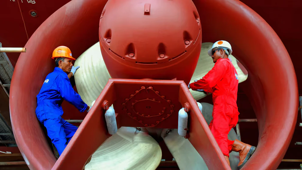 Two workers in blue and red overalls are working on a reactor in a hangar.