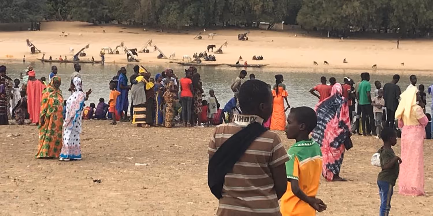 People wearing brightly coloured clothing standing on the bank of the Senegal River which separates Senegal and Mauritania.