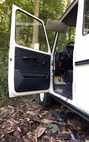 A green mine lying on the ground next to the open door of a white jeep