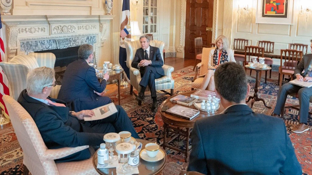 Six people sitting in a circle around a small wooden table, including Federal Councillor Ignazio Cassis talking to US Secretary of State Anthony Blinken.