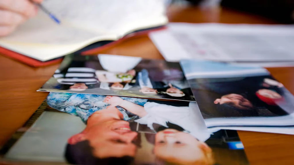 Family photos are placed on a table with a person filling in an ICRC form in the background.