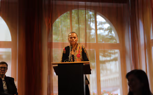 Patricia Danzi, Head of the Swiss Agency for Development and Cooperation stands at a lectern and speaks to diplomatic representatives in the hall.