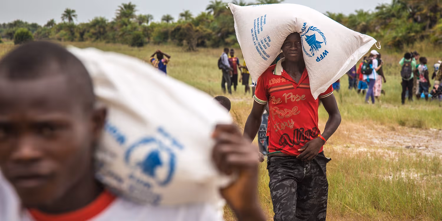 Two men carry bags of food on their shoulders and head.