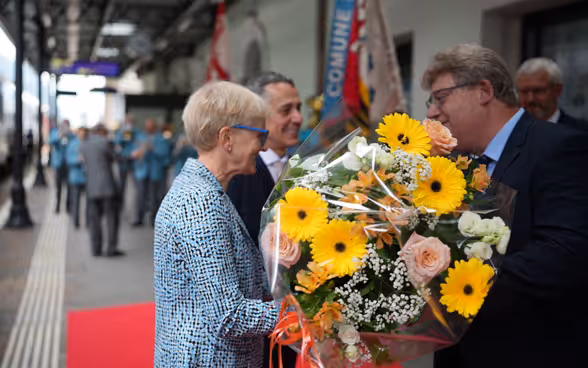 On the platform of the Biasca railway station, Paola Cassis receives a bouquet of flowers from the mayor.