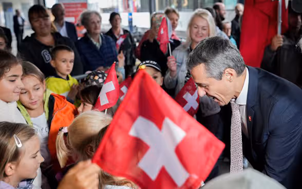 The platform at Airolo railway station is packed with people welcoming the special train. Federal President Ignazio Cassis greets the present people while schoolchildren wave Swiss flags.