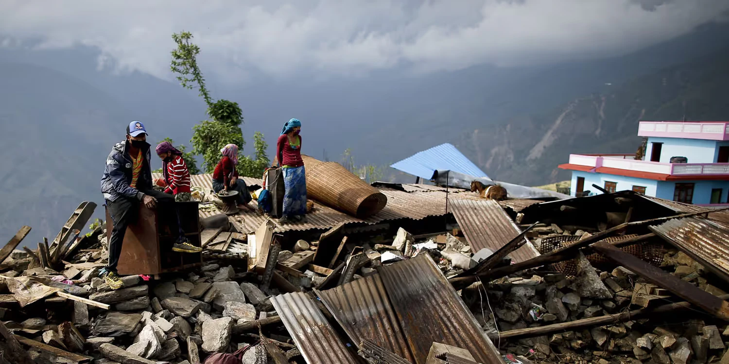 A Nepalese family with two children sits on the ruins of their house in a village in the mountains.
