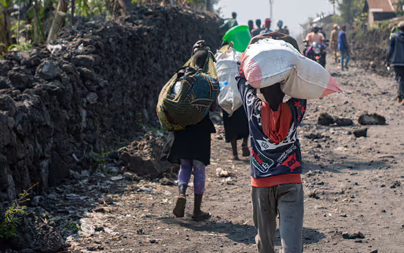 Congolese children walk along a road carrying their belongings on their heads.