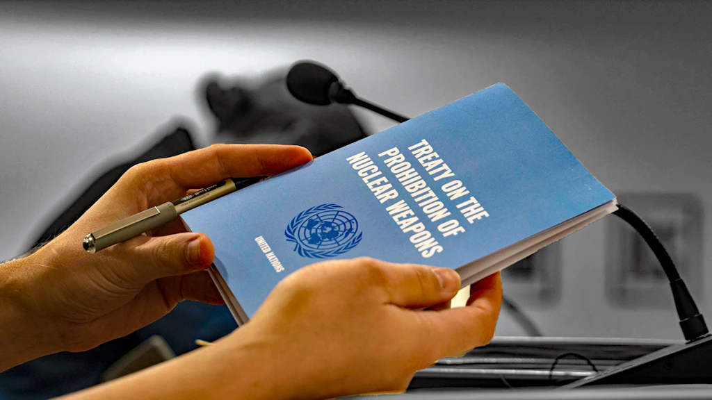On holding a UN brochure about the nuclear weapons ban treaty at a lectern with a microphone. 