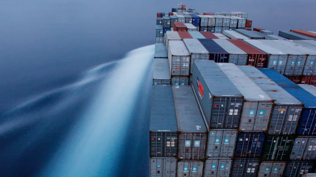A boat carries piles of containers. Water in the background.