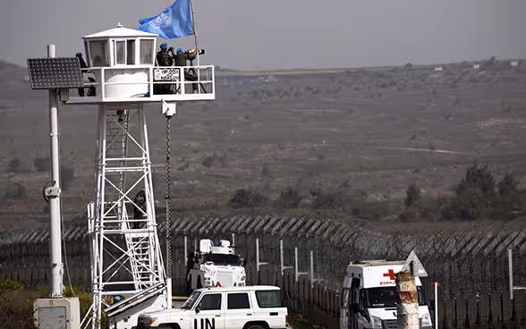 A UNDOF watchtower next to a barbed wire fence in a barren area.