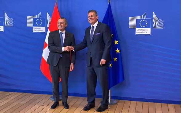 Ignazio Cassis and Maroš Šefčovič shake hands. The Swiss and European flags are in the background.
