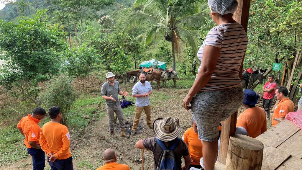 A group of people wearing orange T-shirts are listening to an expert in Colombia.
