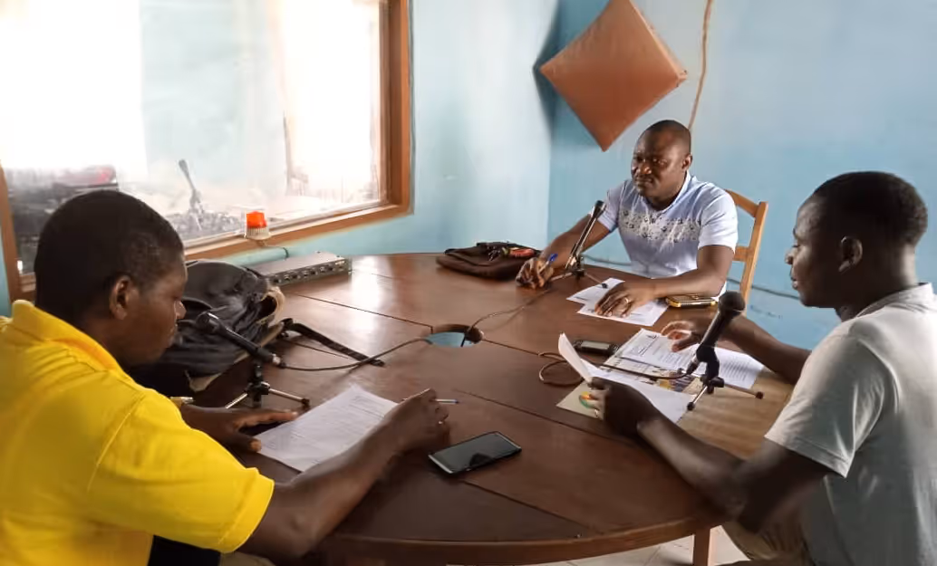 Three men with microphones around a table taking part in a radio discussion. 